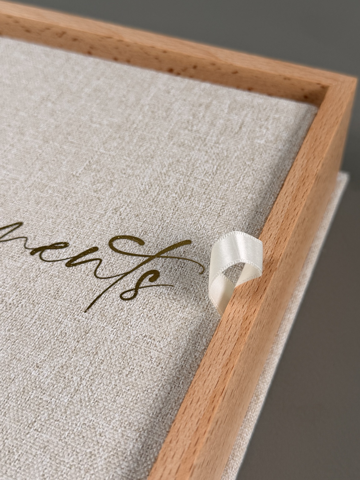Diagonal detail of a wooden presentation box, linen lining and lifting ribbon
