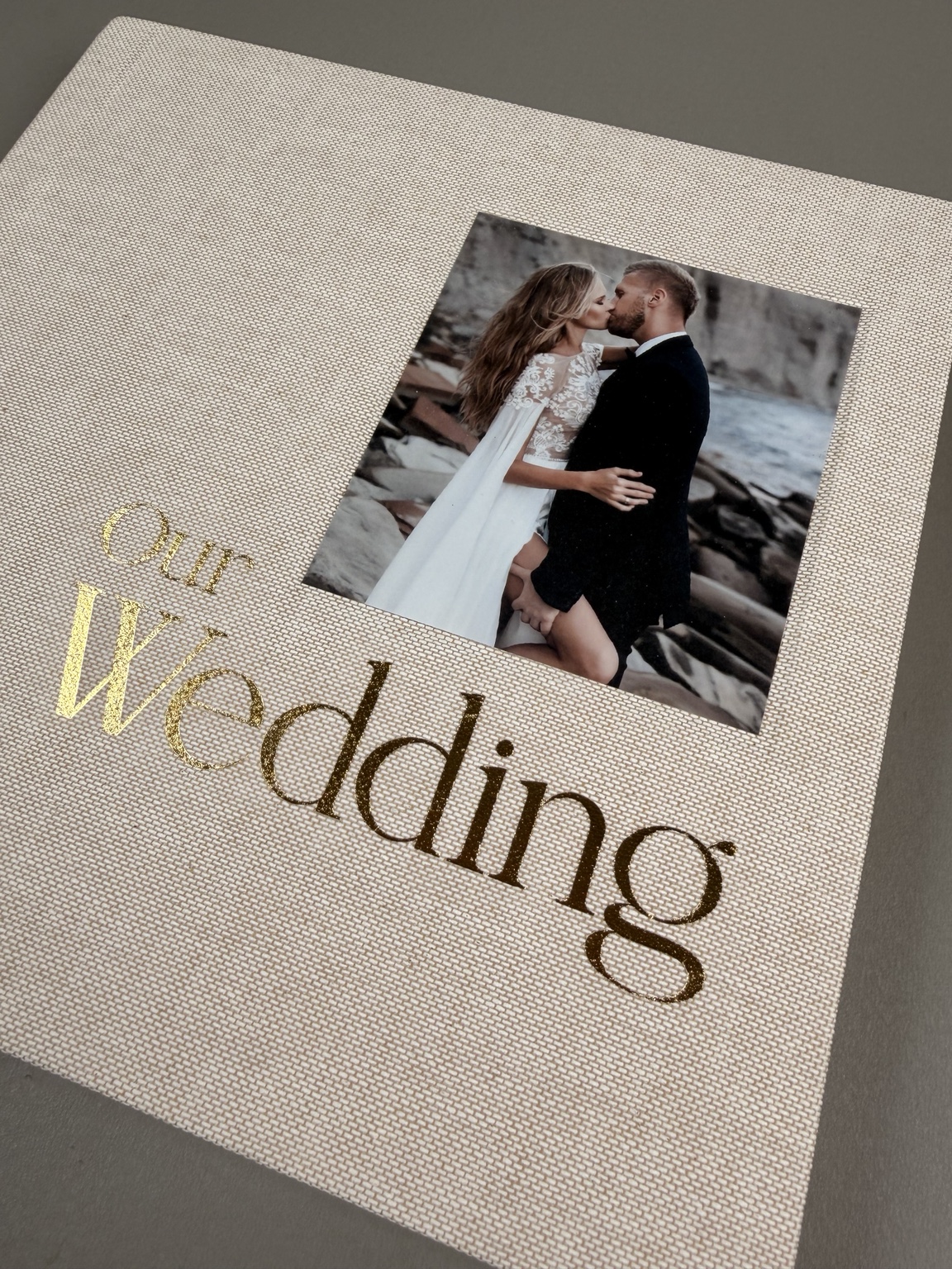 Diagonal detail of ivory linen, a recessed wedding photograph and gold foil lettering